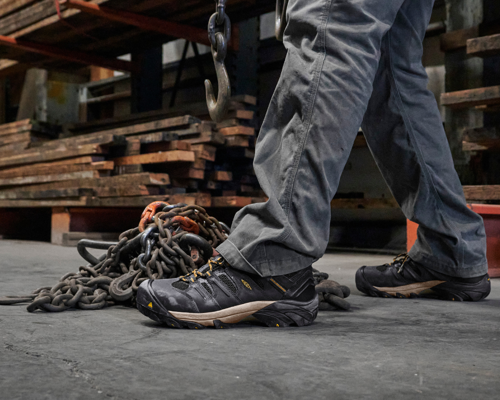 Warehouse worker walking on concrete floor wearing ASTM-rated work boots for safety and comfort in an industrial environment.