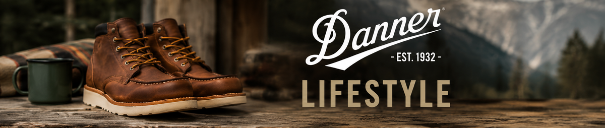 Danner brown leather lace-up lifestyle boots beside a green mug, with mountains and forest behind.