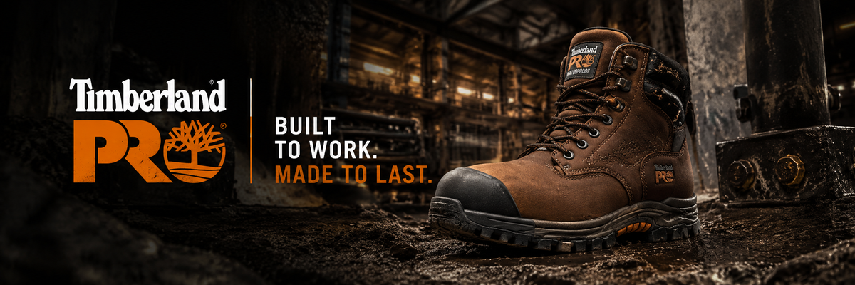 Timberland PRO work boot in brown leather with a black toe cap, shown in a dark industrial setting with Timberland branding and the slogan 'Built to work. Made to last.